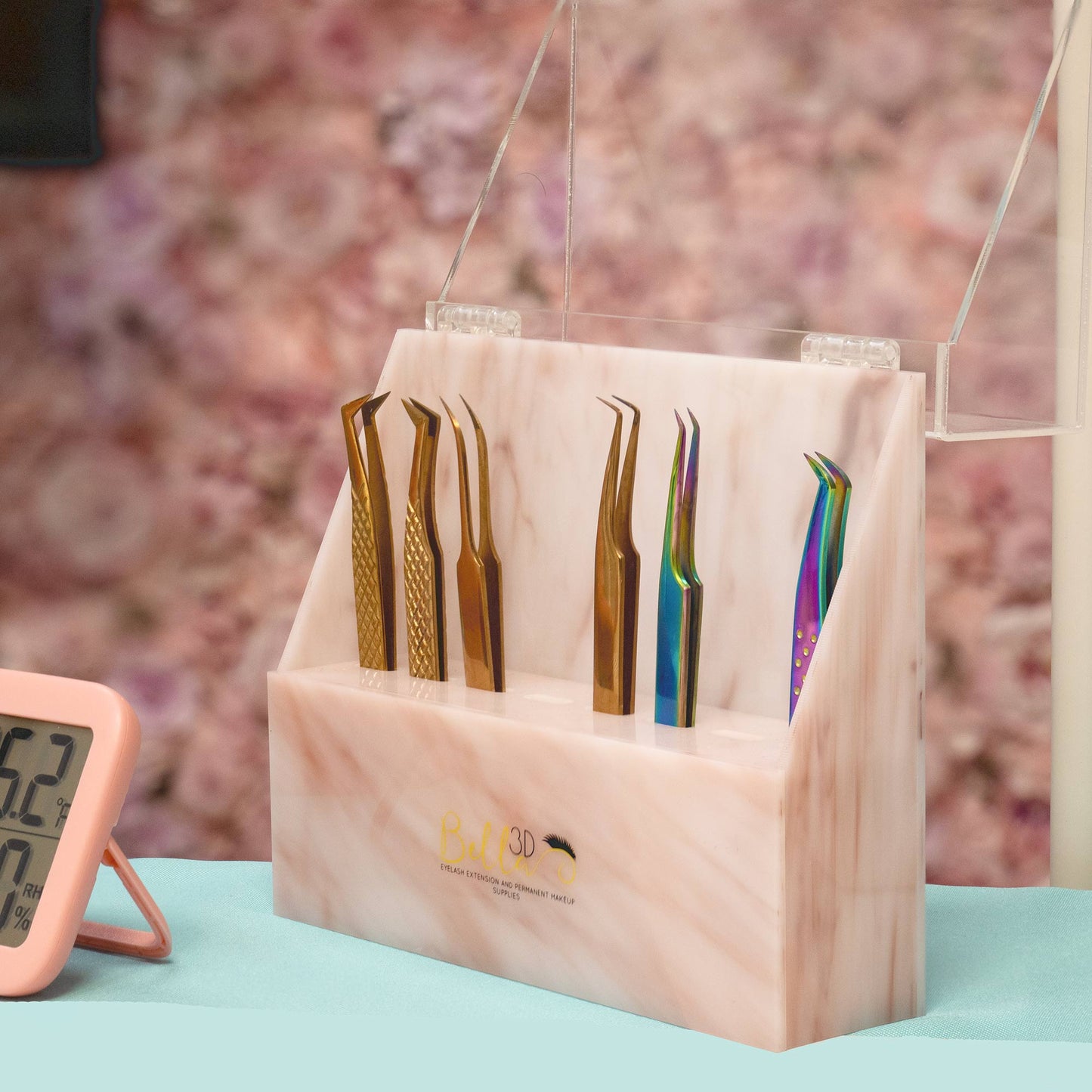Acrylic Tweezer Stand holding six eyelash extension tweezers in metallic and rainbow finishes on a pink marble base.