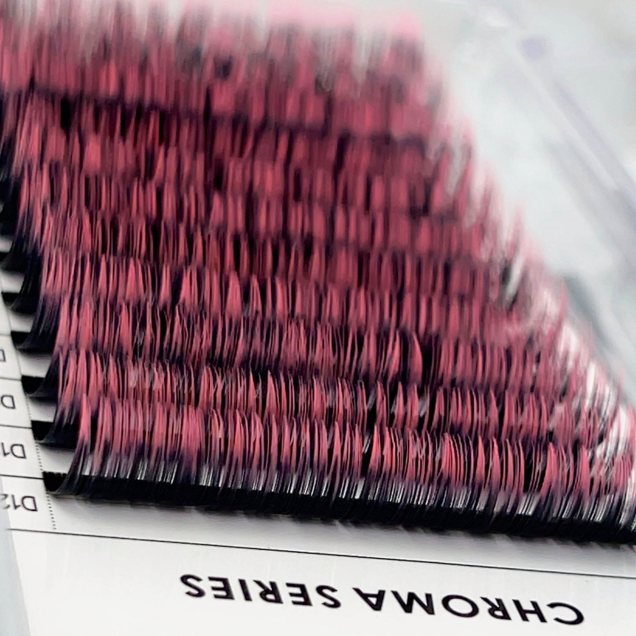 Close-up of Chroma Ombré - 0.07 pink and black eyelash extensions neatly arranged in a tray