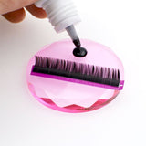 Close-up of a hand applying adhesive on Crystal Lash Glue Stones with eyelash extension supplies on top.
