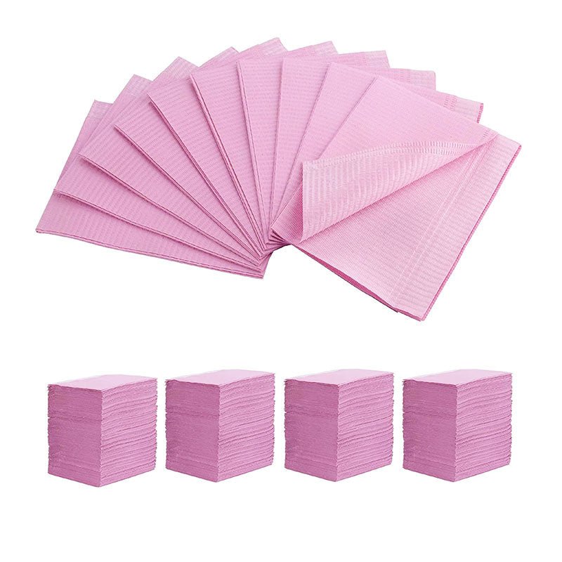 Pink disposable Dental Bibs arranged fanned out and stacked in four neat piles for dental use.